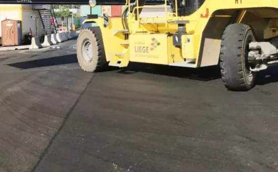 Chantier de voirie avec compacteur en action finissant une couche d’enrobé, signalisation et aménagements de sécurité présents.