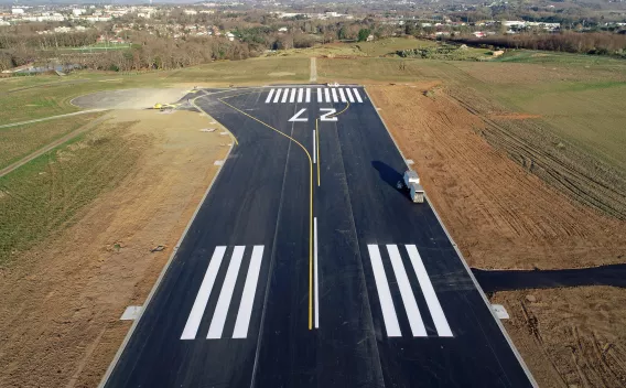 Aéroport de Biarritz : Piste nouvellement réalisée en environnement rural, marquages 27 et barres d’approche impeccables, bretelle de sortie tracée et plateformes latérales prêtes pour l’équipement aéronautique.