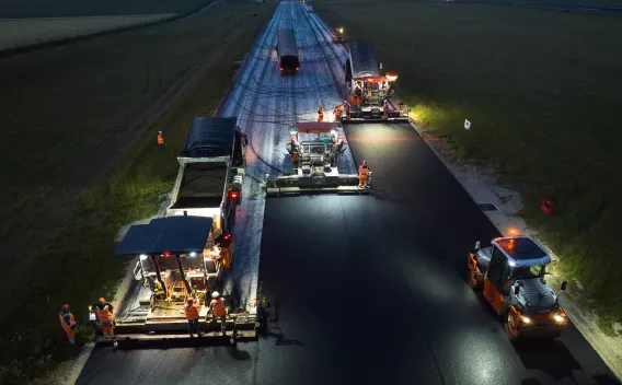 Aéroport de Beauvais : Chantier nocturne d'enrobé en pleine action : pelleteuses et finisseurs synchronisés sous projecteurs, déroulant une nouvelle chaussée lisse et régulière au cœur du paysage.