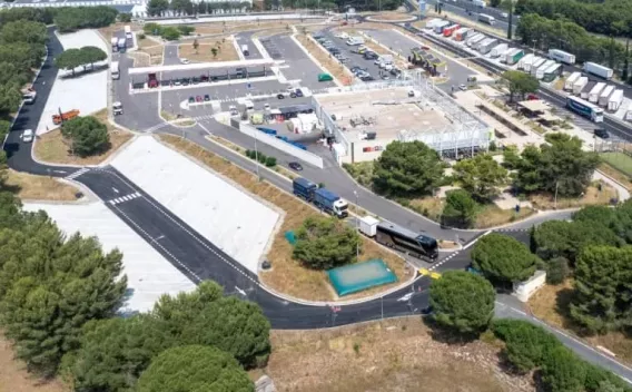 Chaussée neuve menant à une galerie urbaine, surface d’enrobé fraîche avec marquages provisoires et dispositifs de signalisation.