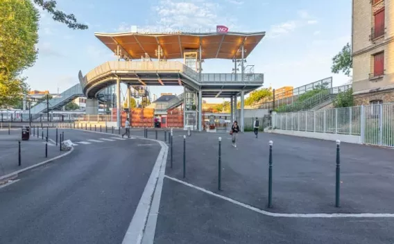 Gare d'Ivry-sur-Seine, génie civil par Colas France : Parvis de gare réaménagé, voiries et trottoirs neufs avec mobilier urbain, accès PMR aux passerelles et au bâtiment voyageurs sous auvent contemporain.