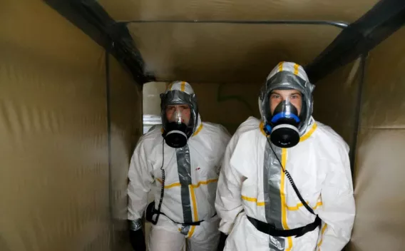 Deux opérateurs en tenue de protection intégrale et appareils respiratoires effectuant une inspection ou préparation d'intervention dans un espace confiné sécurisé.