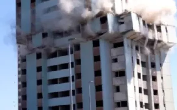 Vérinage de Belfort par Premys filiale de Colas : Dynamitage contrôlé : implosion d’une tour d’habitation en béton avec charges au niveau intermédiaire, panaches de poussière latéraux et périmètre de sécurité dégagé en pied d’ouvrage.