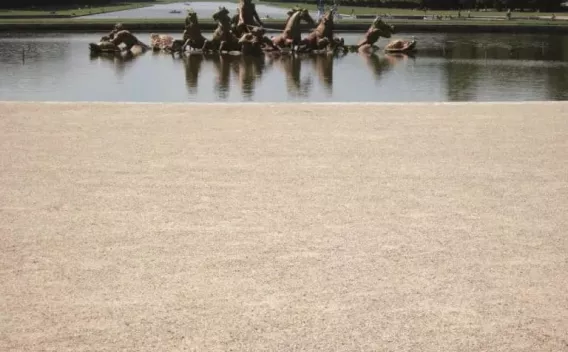  Bassin et groupe sculpté en avant-plan avec allée gravillonnée et perspective aquatique bordée de haies, atmosphère calme.