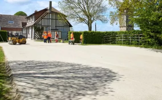 Allée dégagée bordée de bâtiments à colombages et d'ouvriers en tenue haute visibilité, perspective douce sous un ciel clair.