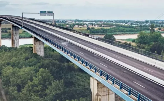 Viaduc moderne à tablier continu, perspective plongeante montrant la chaussée vide s’éloignant vers l’horizon au-dessus d’un terrain boisé et d’un fleuve.