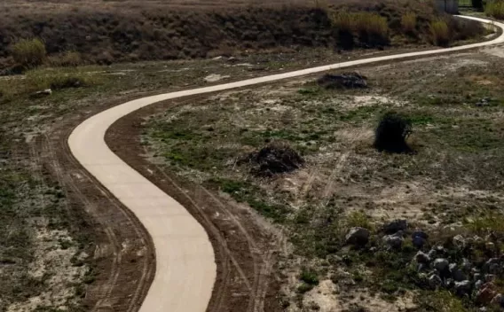 Cheminement neuf en enrobé clair serpentant dans un terrain naturel semi-aride : ruban continu aux bords nets, talus et végétation clairsemée autour, tracé sinueux s’éloignant vers l’horizon.