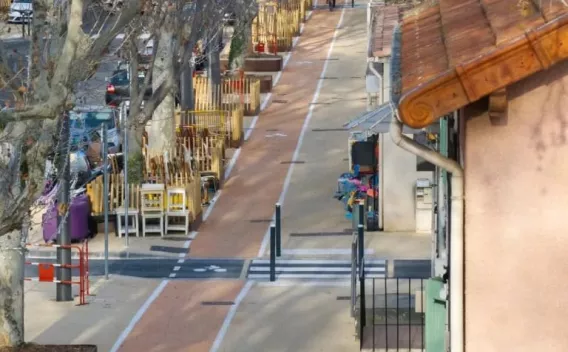 Aménagement urbain avec piste piétonne et mobilier de terrasse le long d'une voie, intégrant signalisation et séparateurs pour sécurité des usagers.