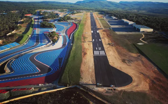 Vue aérienne d'un complexe combinant circuit sportif aux bandes colorées et une piste d'aviation rénovée, alignement précis des marquages et aménagements périphériques pour usage mixte et haute performance.