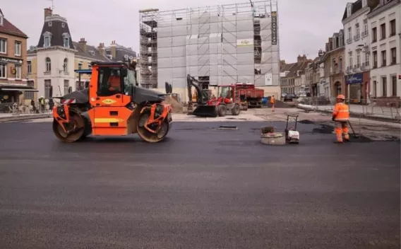Chantier urbain de rénovation de chaussée avec rouleau compacteur en cours de finition d’une couche d’enrobé, opérateurs en haute visibilité et balisage de sécurité.