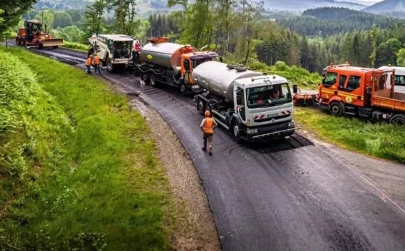 Chaîne d’engins et camions de pose d’enrobé opérant sur une route en milieu rural, coordonnant application et compactage pour un revêtement uniforme et durable.