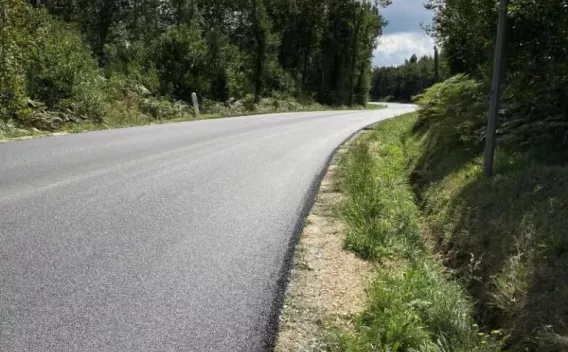 Pose d’enrobé fraîche sur route rurale sinueuse, bordures stabilisées en grave non traitée, accotement végétalisé et environnement boisé; surface uniforme prête à la mise en signalisation.