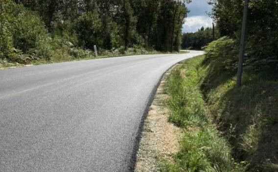 Pose d’enrobé fraîche sur route rurale sinueuse, bordures stabilisées en grave non traitée, accotement végétalisé et environnement boisé; surface uniforme prête à la mise en signalisation.