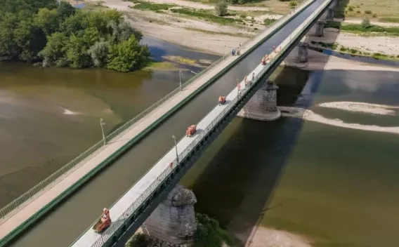 Viaduc sur rivière vu en plongée, tablier étroit piétonnier et routier traversant un paysage alluvial, mise en évidence des piles et de la géométrie longitudinale.
