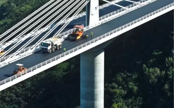 Revêtement en enrobé posé par finisseur sur tablier de pont avec circulation réglée et compactage.