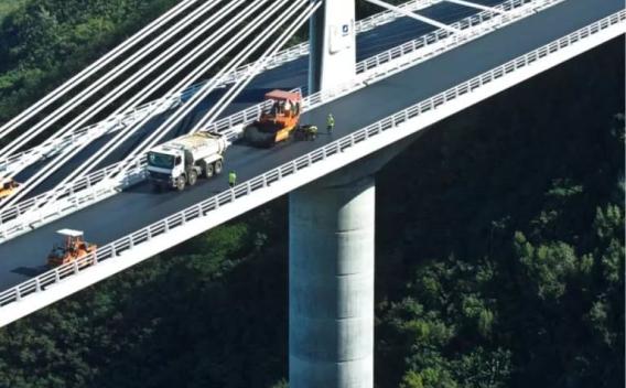 Revêtement en enrobé posé par finisseur sur tablier de pont avec circulation réglée et compactage.