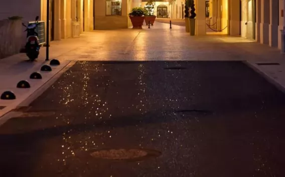 Revêtement urbain humide éclairé le soir, mettant en évidence l'adhérence du bitume et l'esthétique du centre-ville après maintenance.