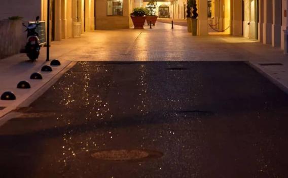Revêtement urbain humide éclairé le soir, mettant en évidence l'adhérence du bitume et l'esthétique du centre-ville après maintenance.
