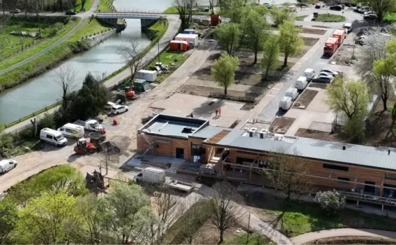 Aménagement paysager et voirie en bord de canal : vue aérienne d’un site en travaux avec bâtiment neuf, voiries internes, stationnements et engins.