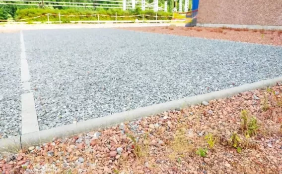 Plateforme drainante en grave compactée, délimitée par des bordures béton, dans un environnement technique paysager.