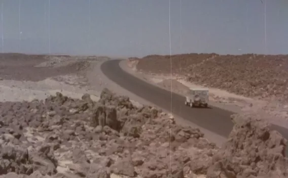 Route asphaltée traversant un paysage désertique rocailleux, avec un véhicule tout-terrain circulant sous un ciel dégagé.