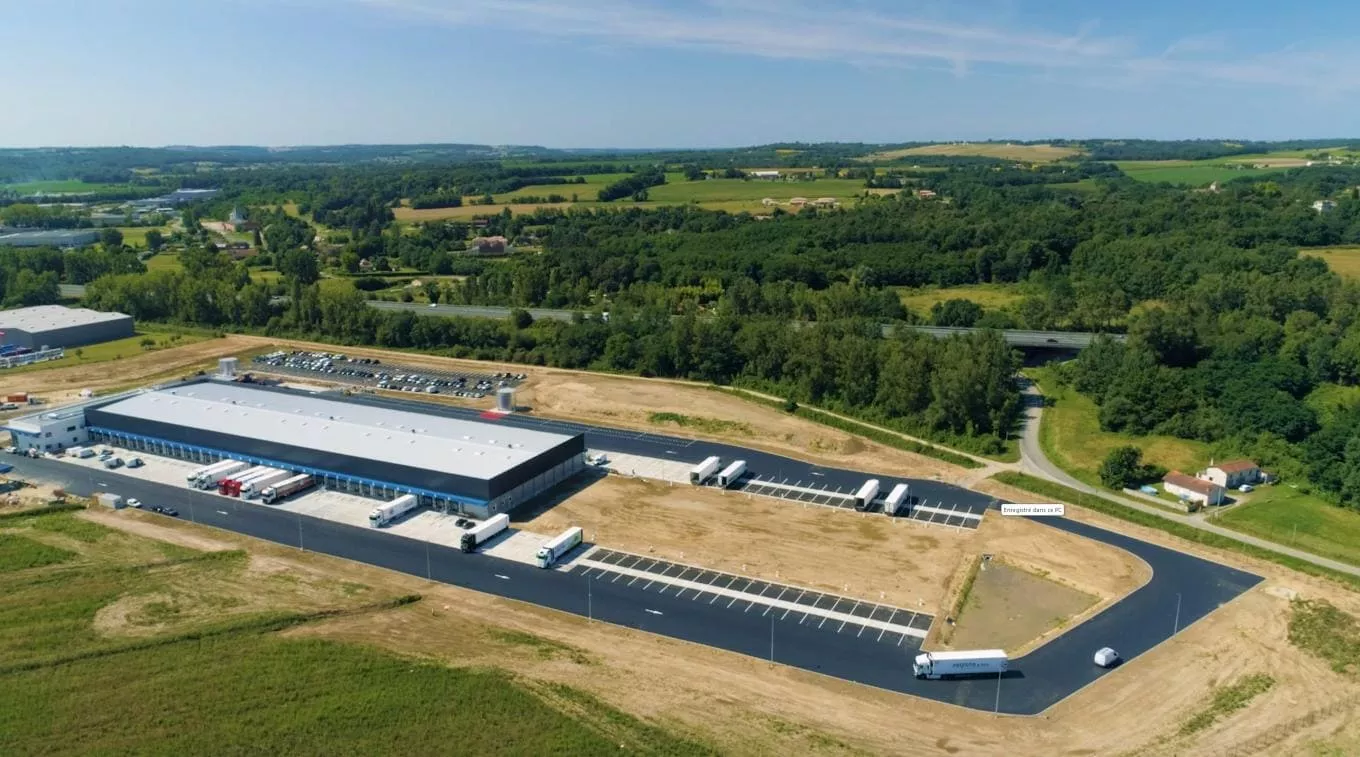 Plateforme industrielle créée par Colas : Vue aérienne d’une plateforme logistique récemment aménagée avec espaces de stationnement pour camions, voirie goudronnée et zones de réception en contexte rural verdoyant.