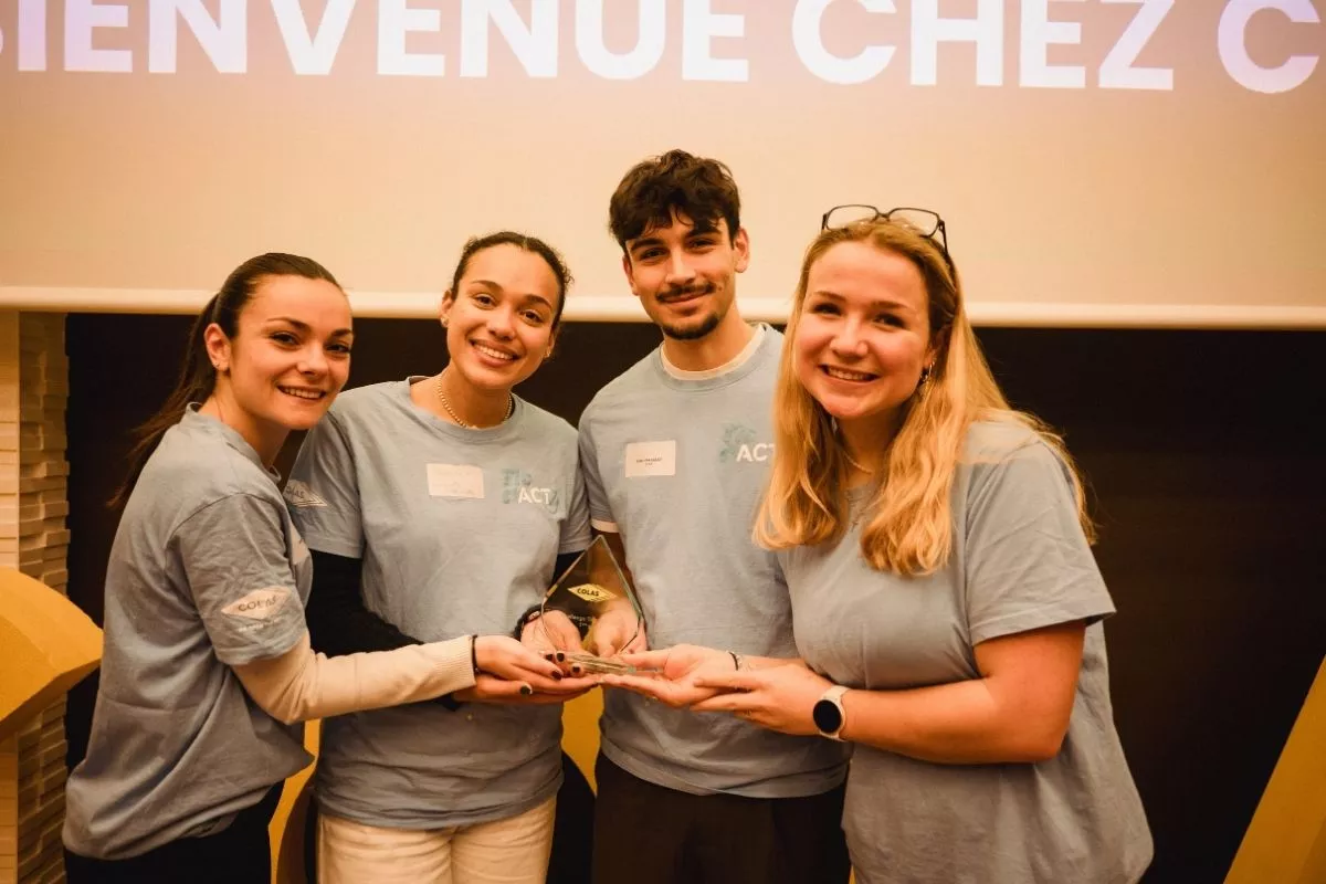 Challenge Tic t'ACT Vainqueurs : Équipe lauréate TIC & ACT posant sur scène avec un trophée, t‑shirts bleus et écran « Bienvenue chez Colas » en arrière‑plan.