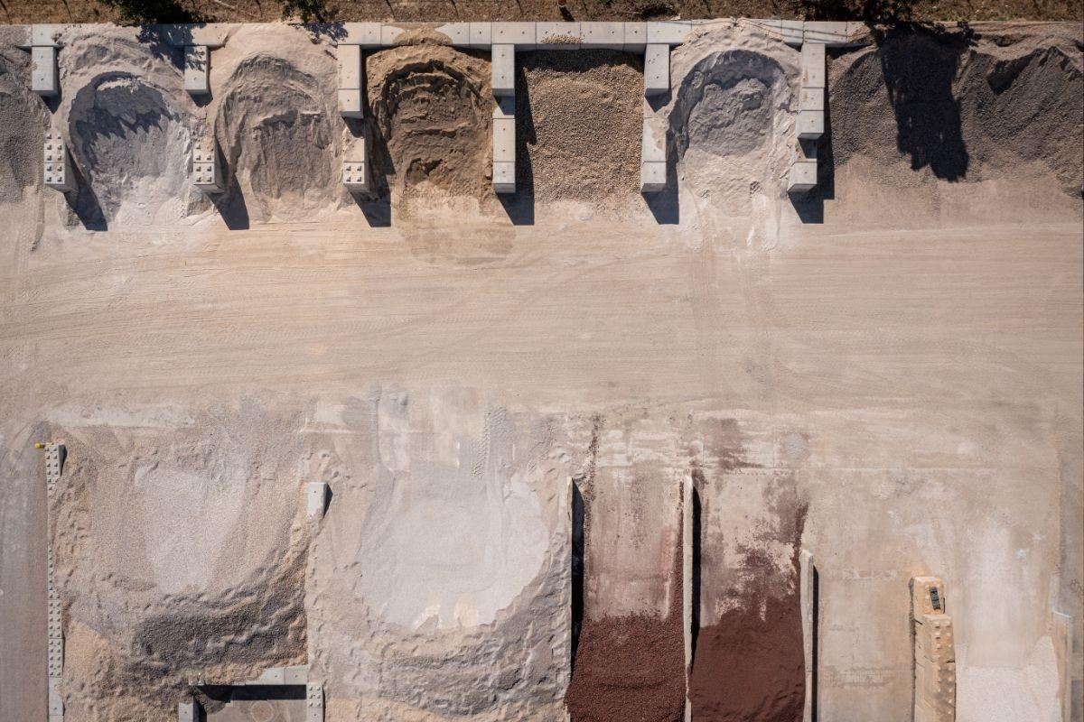 Vue aérienne d’une plateforme de stockage avec plusieurs tas de granulats de différentes couleurs et granulométries, séparés par des murs en béton