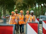 Équipe de chantier en EPI traversant une zone de travaux routiers balisée, coordonnant les opérations au milieu de la circulation.