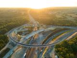 Échangeur autoroutier en travaux au coucher du soleil : vue aérienne d’un chantier de reconfiguration avec bretelles neuves, remblais en cours, circulation maintenue sur les voies centrales.