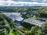 Plateforme industrielle par Colas : Aménagement commercial en lisière forestière : centre commercial moderne avec vastes parkings, voiries d’accès et talus paysagers — intégration du site dans un relief vallonné, gestion des flux et des eaux pluviales.