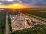Vue aérienne d’un vaste chantier fondations en cours d’excavation et de terrassement au lever du soleil, bordé d’une route et d’une forêt.