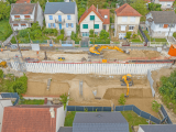 Chantier urbain de rénovation d’un talus et d’une voirie en excavation, avec palplanches, pelleteuses et matériel de terrassement entre maisons individuelles.