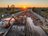 Chantier ferroviaire au coucher du soleil avec pelles hydrauliques en action pour la déconstruction de la plateforme voie, arrosage anti-poussières et circulation maintenue en latéral sur voiries adjacentes.
