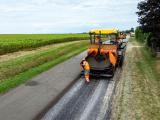 Application d'une couche de roulement par gravillonnage sur route de campagne : épandage du liant puis distribution de gravillons depuis le finisseur, engins et équipes en ligne.