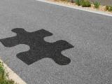Patchs d'enrobé contrastés formant un motif puzzle sur une section de route rurale, illustrant une intervention localisée de réparation ou d'enduction ciblée.