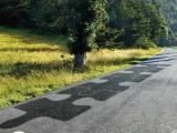 Patchs d'enrobé contrastés formant un motif puzzle sur une section de route rurale, illustrant une intervention localisée de réparation ou d'enduction ciblée.