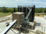 Vue aérienne d'une carrière en terrasses avec zones de concassage, stockage et une centrale de traitement en plan rapproché, intégrée dans un paysage agricole et boisé.