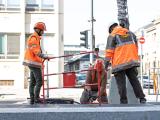 Trois ouvriers en tenue haute visibilité travaillent en sécurité autour d’un chantier urbain avec barrières et matériel de manutention pour interventions sur voirie.