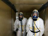 Deux opérateurs en tenue de protection intégrale et appareils respiratoires effectuant une inspection ou préparation d'intervention dans un espace confiné sécurisé.