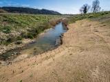 Génie écologique - Théziers par Colas : Berge de cours d’eau stabilisée par tapis de coco et nombreux piquets, talus végétalisé en rive opposée, paysage naturel vallonné sous ciel clair.