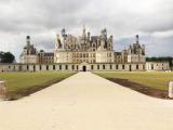 Château Renaissance vu de face, cadrage symétrique avec une allée centrale menant à la façade majestueuse sous un ciel nuageux.