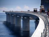 Travaux d’enrobé sur un tablier de pont au-dessus de la mer : finisseurs et compacteurs en œuvre, zone de chantier balisée et revêtement neuf posé sur la chaussée du pont.