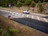 Section de route en cours de rénovation avec couche d’enrobé neuve en accotement, marquages provisoires et cône de chantier, dans un environnement boisé.