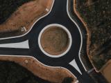 Rond-point réalisé par Colas : Giratoire neuf vu en plongée, chaussées en enrobé noir avec îlot central engazonné et triangles de bétons blancs aux bretelles, inséré dans un paysage terreux en cours d’aménagement.