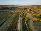 Génie écologique par Colas à Théziers : Vue aérienne professionnelle d’un paysage agricole vallonné avec une voie sinueuse et des parcelles labourées au coucher de soleil, illustrant circulation, drainage et structuration du territoire.