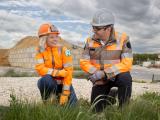 Portrait de collaborateurs Colas : Équipe de chantier en discussion sur site d’infrastructure, équipée d’EPI complets (casques, gilets haute visibilité, gants), illustrant coordination, sécurité et suivi de travaux.