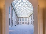 Rénovation du château de Villers-Cotterets par Colas : Cour historique cadrée par un porche voûté, s’ouvrant sur une cour pavée sous une verrière métallique ajourée, fusionnant pierre chaude et structure contemporaine.