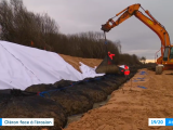 Oléron face à l'érosion : Chantier de lutte contre l’érosion littorale à Oléron : pelle hydraulique posant des boudins/géotextiles en file le long d’une dune protégée par un géotextile blanc, équipe en gilets haute visibilité, plage atlantique et mer à droite.