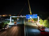 Pose de nouveaux panneaux de signalisation sur portique au-dessus de l'autoroute A9 lors d'une intervention de nuit.